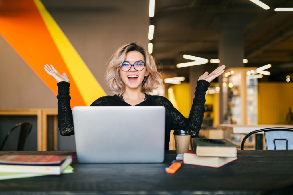 Smiling woman with a laptop raising her hands in excitement, representing a therapist whose website is kept alive and responsive with ongoing maintenance