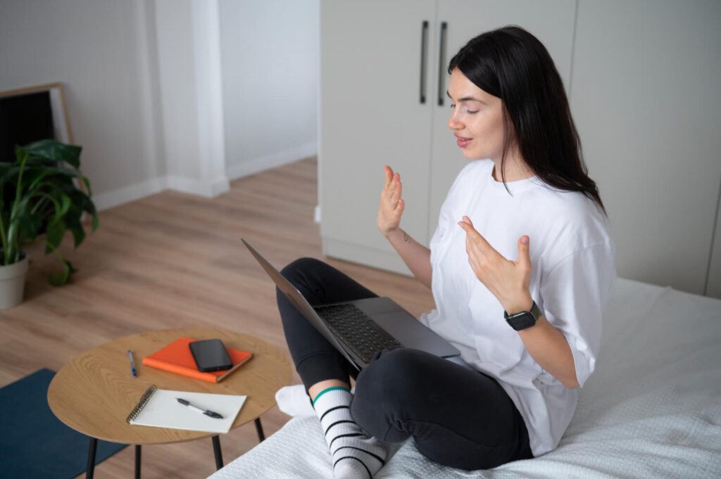 Woman sitting on her bed talking on a laptop video call, representing a therapeutic digital narrative shared through an online therapy website