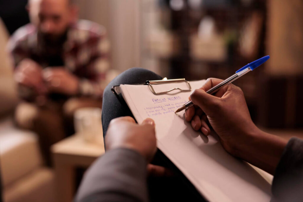 Therapist writing patient records during a counseling session, representing mental health websites that help clinicians care for more people